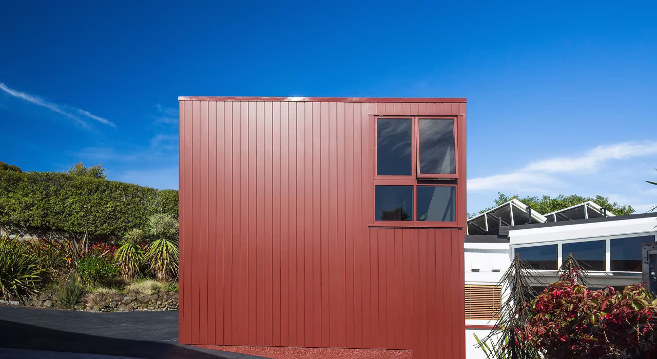 <img alt="Exterior detail of red Coloursteel cladding with small square window, set among established garden planting." src="/images/s/i/t/e/-/site-architects-interior-architecture-modernist8-863929b7.webp" width="2560" height="1707" />