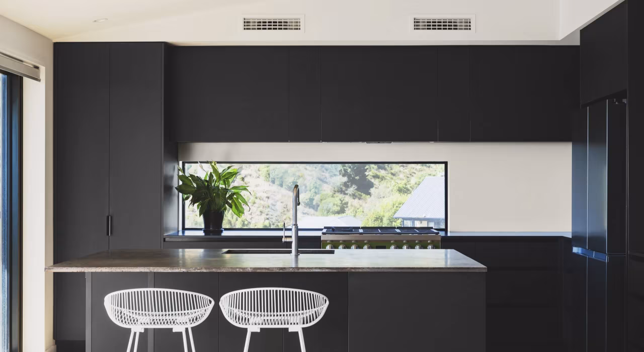 <img alt="Dark kitchen with island bench, white stools and a window framing the landscape outside." src="/images/s/i/t/e/-/site-architecture-drayton-drive11-14308f5c.webp" width="2560" height="1706" />